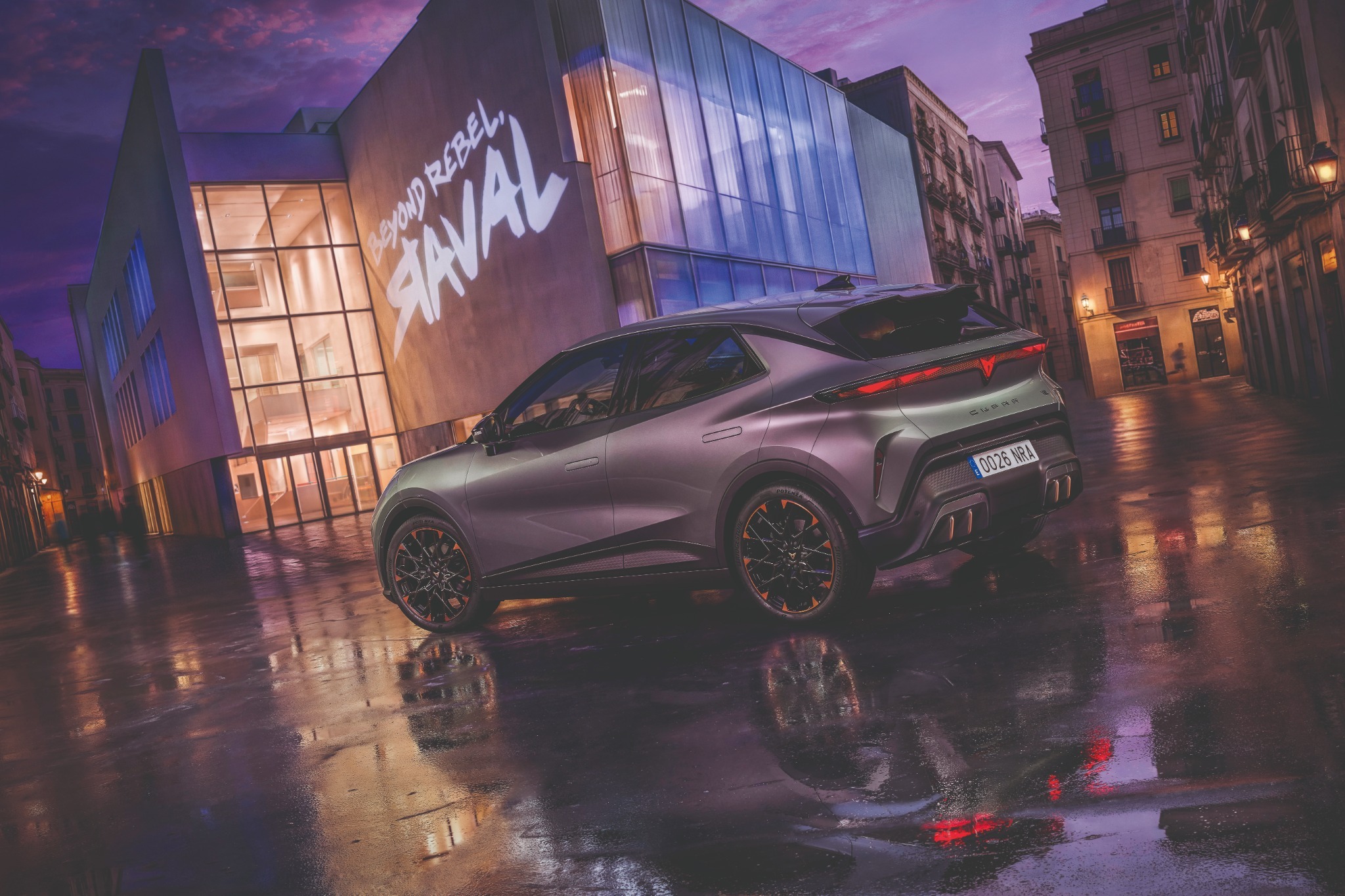 Cupra Raval électrique stationnée devant un bâtiment illuminé dans une ambiance urbaine nocturne