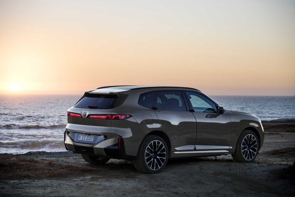 BMW iX5 60 xDrive vue de trois-quarts arrière au coucher du soleil en bord de mer