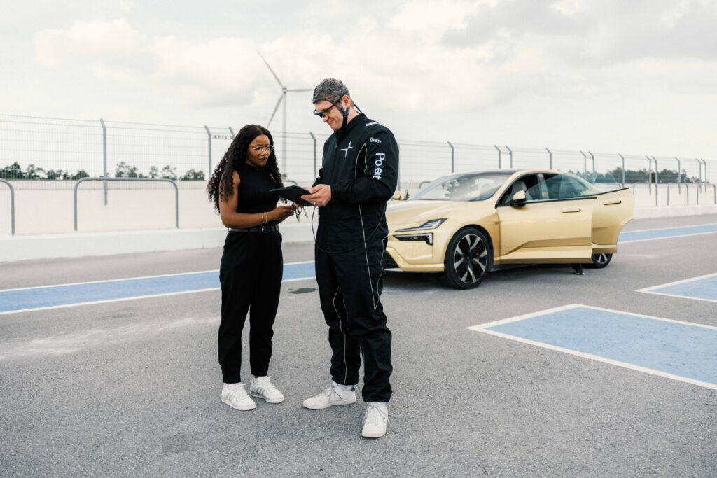 Deux membres de l’équipe discutent près d’une voiture dorée, portière ouverte, sur une piste (photo officielle Polestar)