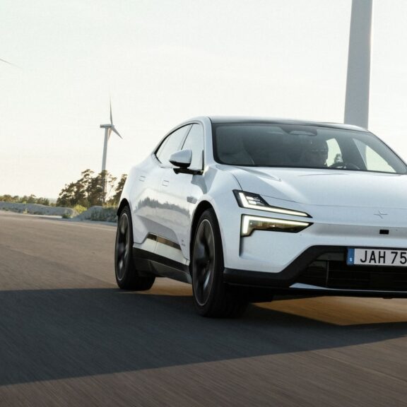 Polestar 4 blanche en roulage sur une route dégagée, avec des éoliennes en arrière-plan (photo officielle Polestar)